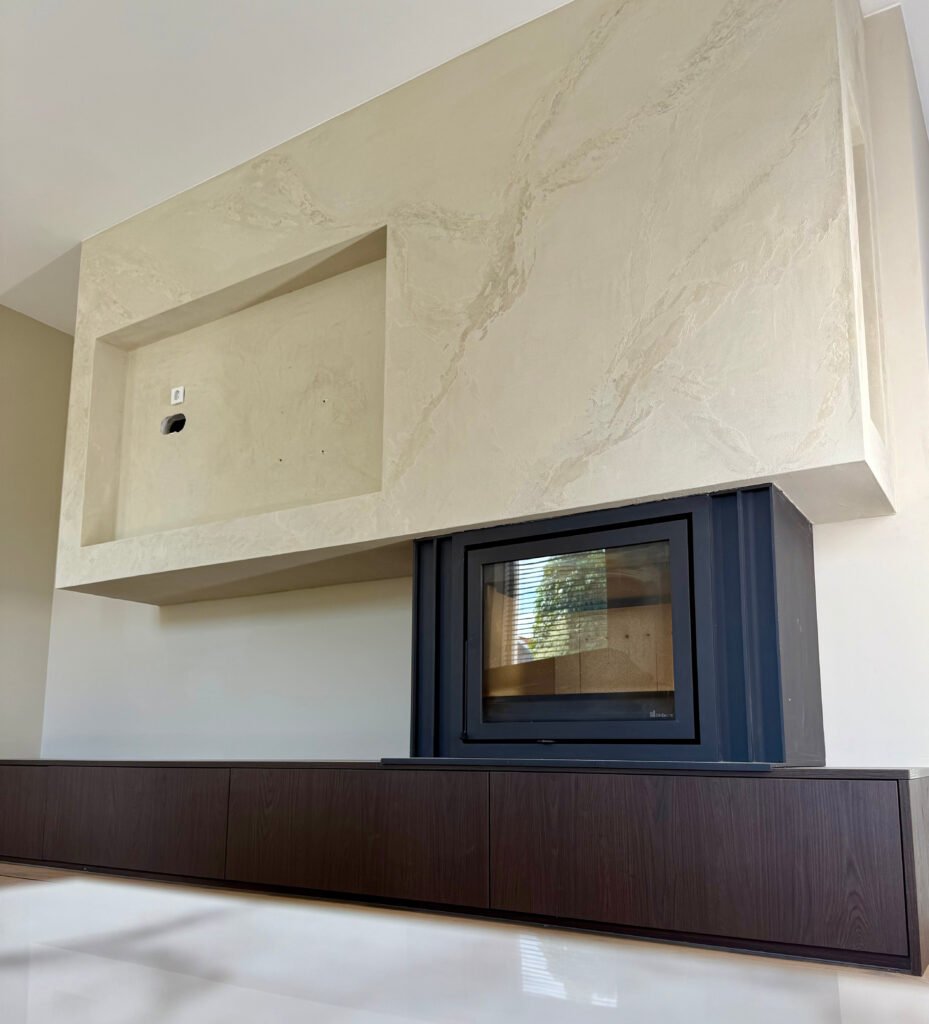 Cinewall met inbouwhaard en TV-nis, afgewerkt in handmatig aangebracht travertinlook sierstuc, met strak gespoten wanden en plafonds – gerealiseerd door LenKraft in Twente